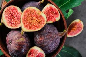 Fresh figs and fig halves on a brown old clay plate. Dark background, close-up top view. Seasonal ripe fruits, mediterranean diet photo
