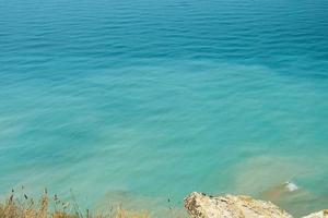 Blurred background, view of the sea in the midday heat from the rocky shore. Hot summer vacation, pastel colors and reflections on the water. Abstract blur poster or advertising banner photo