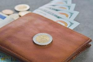 Euro coin and us dollar banknotes in a brown leather wallet on a gray table background, close-up, selective focus, blurred background, business finance concept photo