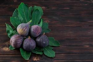 Several ripe figs on fig tree leaves on an old wooden table, horizontal frame with copy space. Seasonal fruits, harvest background or mediterranean diet articles photo