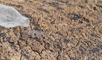 Selective focus of dry cracked earth due to drought, water is poured from a plastic bottle, crisis and drought in Asia, critically hot summer, lack of water photo