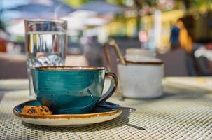 Steam rises over a cup of espresso coffee, a glass of water and cookies on the table, close-up, sunlight and selective focus, empty space, cafe breakfast, advertising or banner photo
