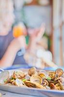 Blurred background with a dish of boiled vongole clams on a table in a cafe, vertical frame, in the background the silhouette of a woman with a glass of wine. Idea for a screensaver or banner photo