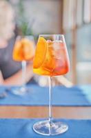 Two glasses with colorful Aperol Spritz cocktail with ice on a dining table in a cafe, blurred bright background, selective focus of a weekend at sea. Refreshing drink. photo