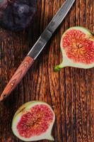 Halves of figs on a wooden table, next to an old knife, top view of the fruit, vertical frame. Ripe fig fruits, mediterranean diet, idea for advertising photo