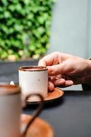 A woman takes a cup of coffee, Turkish black frothy coffee on a black stone table with branches of wild ivy in the background. Vertical frame, selective focus photo