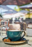 desayuno en un café, toma vertical, el vapor se eleva sobre una taza de café expreso, un vaso de agua y galletas en la mesa, primer plano, luz solar y enfoque selectivo, espacio vacío