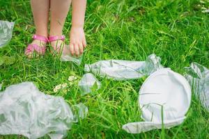 Hand of child cleans green grass from plastic trash photo