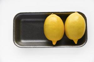 Ripe yellow lemons on a black plastic backing. Delicious lemons from the store on a white background. Yellow lemons packed in a container. photo