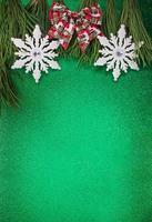 White shiny snowflakes with a bow on fir branches on a green shiny background. Christmas, New Year. Copy space photo