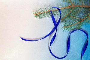 rama de abeto con cinta de raso azul sobre fondo blanco-azul. tarjeta de navidad y año nuevo foto