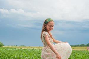 A little girl in a flower dress against the background of rural nature. The joy of a child. photo