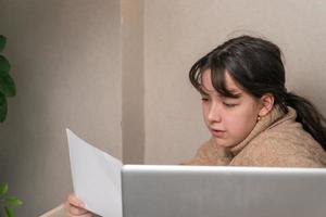 chica trabaja con documentos sentados frente a una computadora portátil en su escritorio foto