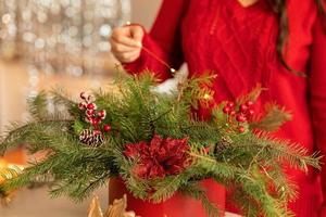 niña recoge un ramo navideño de ramas de abeto, flores y adornos de árboles de navidad foto