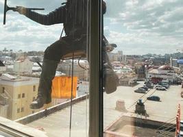 escalador industrial profesional con traje naranja y casco de seguridad lava ventanas sucias con un abrigo de piel fuera de un edificio de oficinas alto a cámara lenta foto