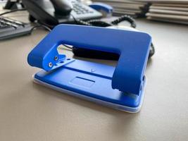 Blue iron metal office punch for punching holes in sheets of paper and documents on the working business table in the office. Stationery photo