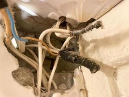 viejos cables retorcidos enredados en telarañas y polvo en un agujero en una pared en un sitio de construcción. electricista industrial muy pobre foto