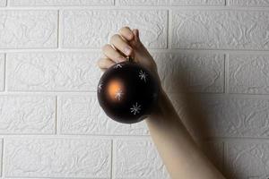 una mano y una bola de árbol de navidad resaltadas en un fondo de pared de ladrillo blanco. foto