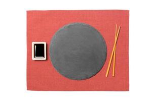 Emptyround black slate plate with chopsticks for sushi and soy sauce on red napkin background. Top view with copy space for you design photo