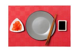 Empty round gray plate with chopsticks for sushi and soy sauce, ginger on red mat sushi background. Top view with copy space for you design photo