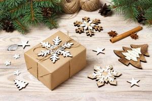 Christmas background with gift boxes wrapped in kraft paper, fir tree branches, pine cones, cinnamon sticks and stars anise on white wooden background photo