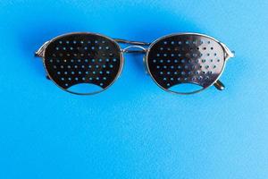 dos tipos diferentes de gafas sobre fondo azul. concepto médico. vista superior. los anteojos negros pinhole ayudan a relajar los ojos cansados aislados en el fondo blanco. anteojos ópticos de moda clásica foto