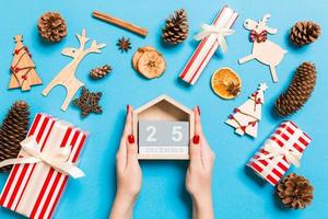 Top view of female hands holding calendar on blue background. The twenty fifth of December. Holiday decorations. Christmas time concept photo