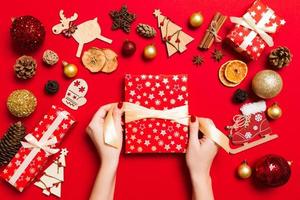 Top view of female hands holding a Christmas present on festive red background. Holiday decorations. New Year holiday concept photo
