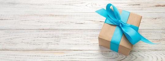 Beautiful gift box with a blue bow on the white wooden table. Top view banner with copy space for you design photo