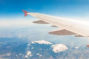 Aircraft wing on the clouds, flies on the mountains background photo