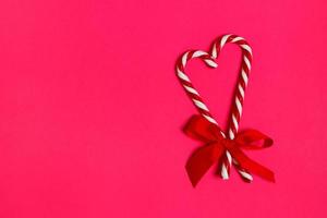 Two Christmas candy canes overlapping to form a heart and a red bow on a pink background. copy space photo