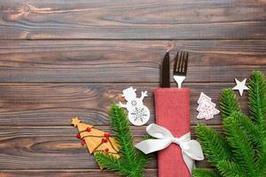 Top view of fork and knife on napkin with christmas decorations and new year tree on wooden background. Holiday and festive concept with copy space photo