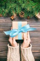 Female hands holding handmade present box in recycled paper on dark wooden table vintage background. christmas preparation concept, Gift wrapping background photo