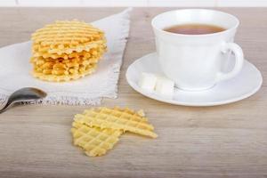 Breakfast with waffles stack on napkin and pieces of waffle with white cup of black tea on wooden surface photo