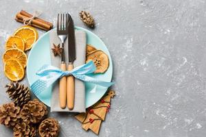 vista superior de la cena festiva decorada con frutos secos y canela sobre fondo de cemento. juego de plato, urensil y adornos de año nuevo. concepto de tiempo de navidad con espacio epmty para su diseño foto