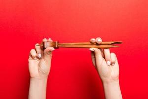 Crop image of two female hands holding chopsticks on red background. Ready to eat concept with copy space photo