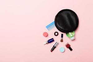 vista superior de los productos de maquillaje caídos de la bolsa de cosméticos sobre fondo rosa. concepto cosmético con espacio para tu diseño foto