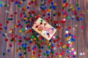 Gift box with star. Creative concept with festive decor on black background. Confetti stars, red, yellow with gift box. Explosion of confetti photo
