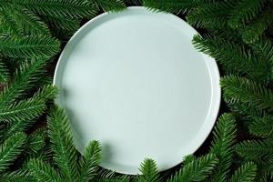 Top view holiday plate among green fir tree branches. Christmas dinner with copy space photo