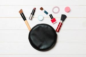 Vista superior de la bolsa de cosméticos con productos de maquillaje derramados sobre fondo de madera. concepto de belleza con espacio vacío para tu diseño foto