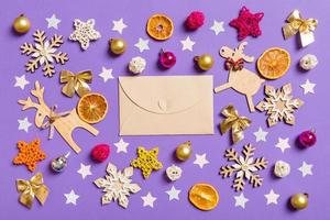 Top view of craft envelope surrounded with New Year toys and decorations on purple background. Christmas time concept photo