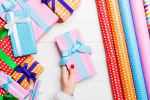 Top view of a woman holding a gift box in her hands on festive wooden background. Rolled up wrapping paper and Christmas decorations. New year time concept photo