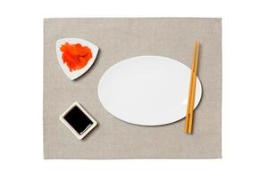 Empty oval white plate with chopsticks for sushi, ginger and soy sauce on grey napkin background. Top view with copy space for you design photo