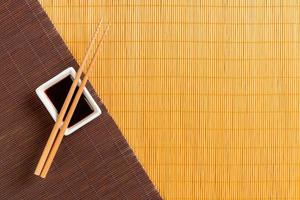 Chopsticks and bowl with soy sauce on two bamboo mat blak and yellow top view with copy space photo