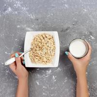 The girl took milk to pour it into oatmeal. Useful and healthy breakfast on a gray background, top view photo