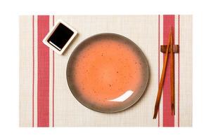 Empty round brown plate with chopsticks for sushi and soy sauce on sushi mat background. Top view with copy space for you design photo