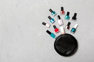 Top view of cosmetics bag with fallen out colourful nail polishes on cement background. Beautiful nails concept with empty space for text photo