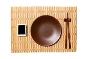 Empty round brown plate with chopsticks for sushi and soy sauce on yellow bamboo mat background. Top view with copy space for you design photo