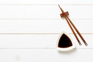 Soy sauce with chopsticks on white wooden table background photo
