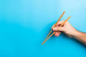 Creative image of wooden chopsticks in male hands on blue background. Japanese and chinese food with copy space photo